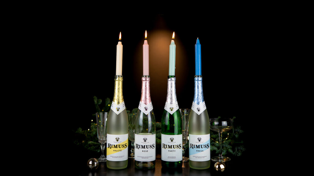 Der Rimuss Adventskranz mit 4 farbigen Kerzen auf den leeren Rimuss-Flaschen. Drei Kerzen brennen.