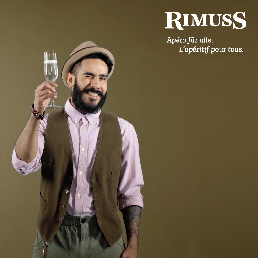 Ein Mann mit Bart, Hut und Hemd steht mit einem Glas Rimuss in der Hand auf dem Plakat.